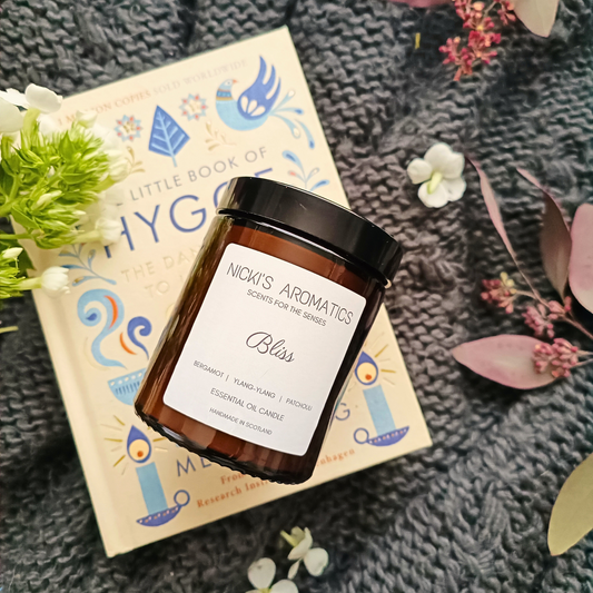 Bliss essential oil candle in an amber glass jar resting on a hygge book and blanket