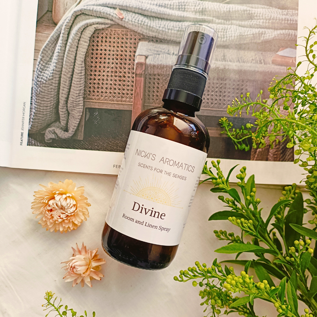 Divine essential oil room and linen spray in a 100ml amber glass bottle resting on an open magazine with flowers