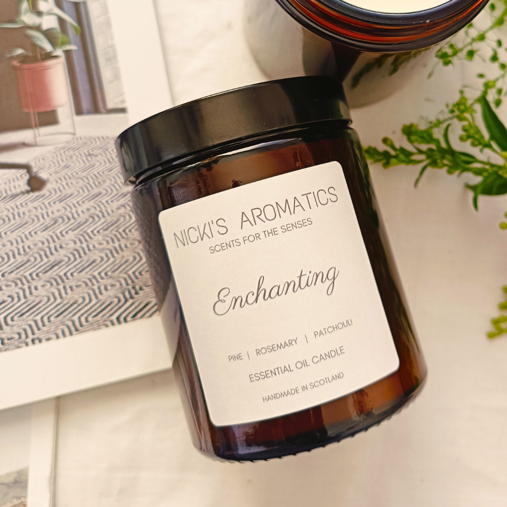 Enchanting essential oil candle in an amber glass jar resting on a white sheet with an open magazine
