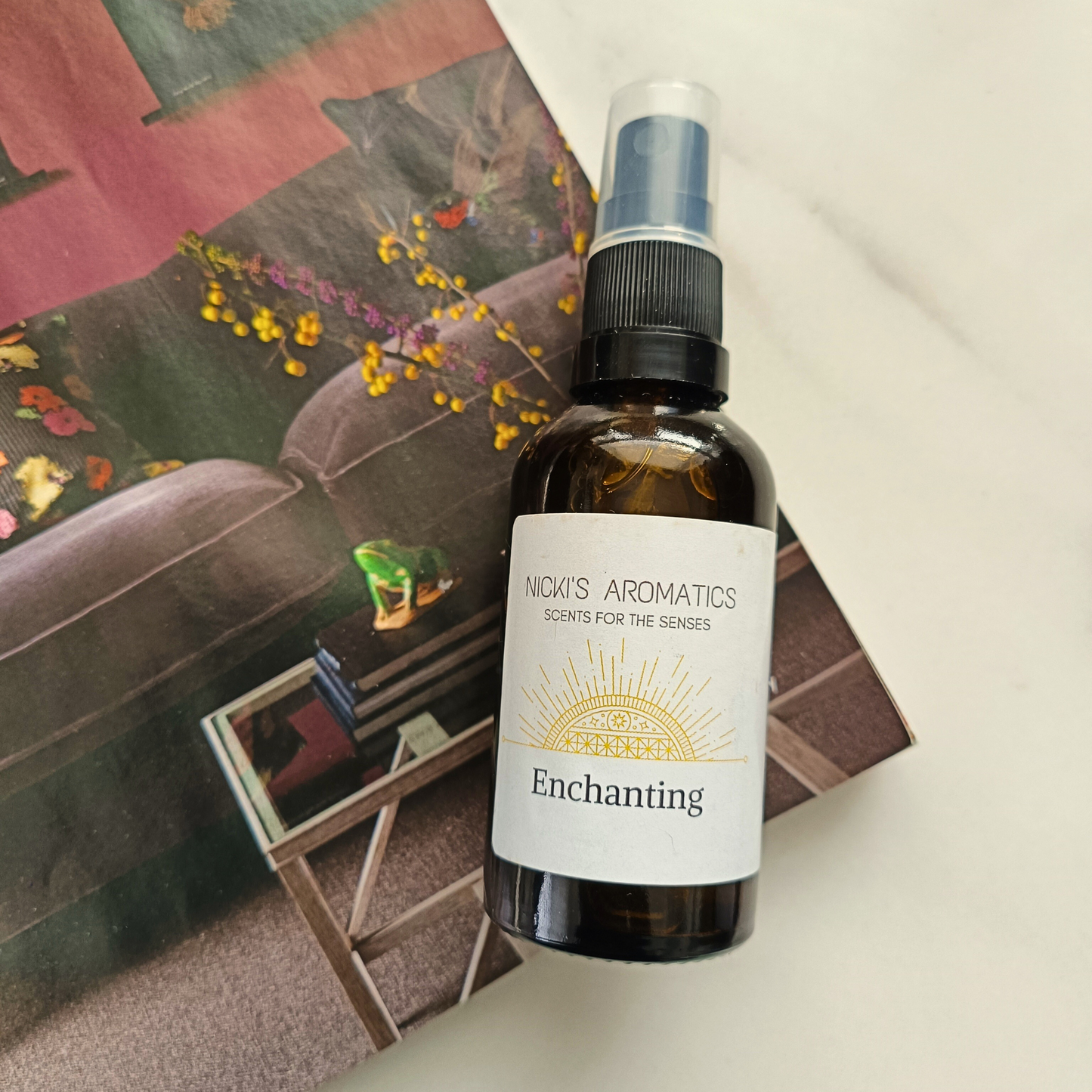 a 50ml amber glass bottle of Enchanting room and linen spray resting on a magazine