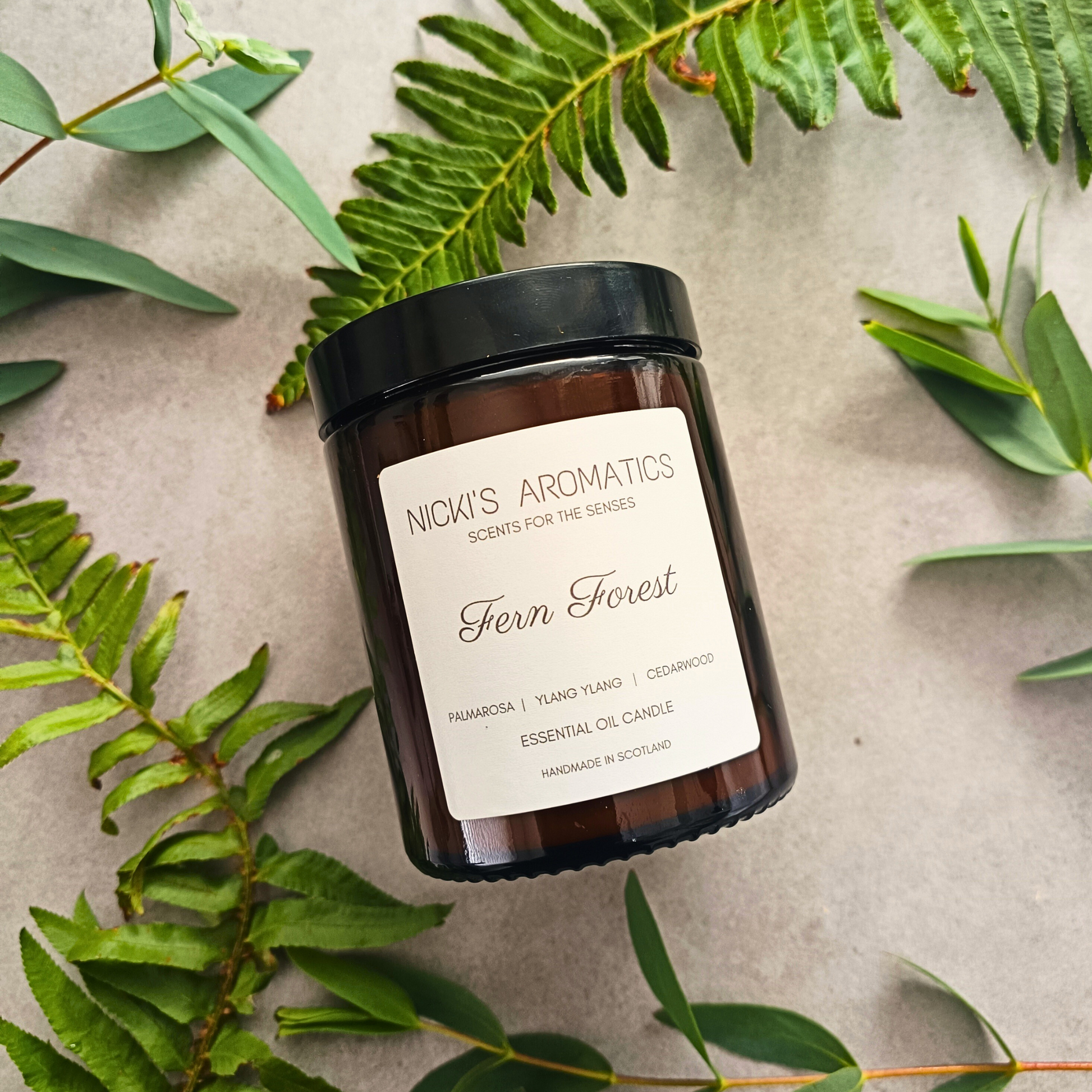 Fern Forest essential oil candle in an amber glass jar surrounded by ferns and leaves