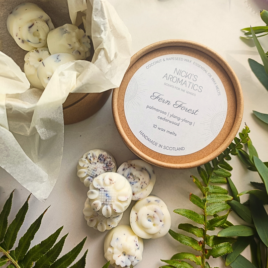 An open tub of Fern Forest essential oil wax melts with some flower-shaped wax melts in the tub and some next to it