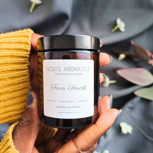 a pair of hands holding a Fern Forest essential oil candle which is in an amber glass jar