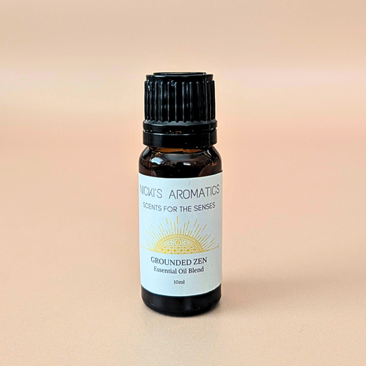 A 10ml amber glass bottle of essential oil blend made with cedarwood, patchouli and citrus. With a black ribbed cap and a white label reading 'NICKI'S AROMATICS' and 'GROUNDED ZEN'.