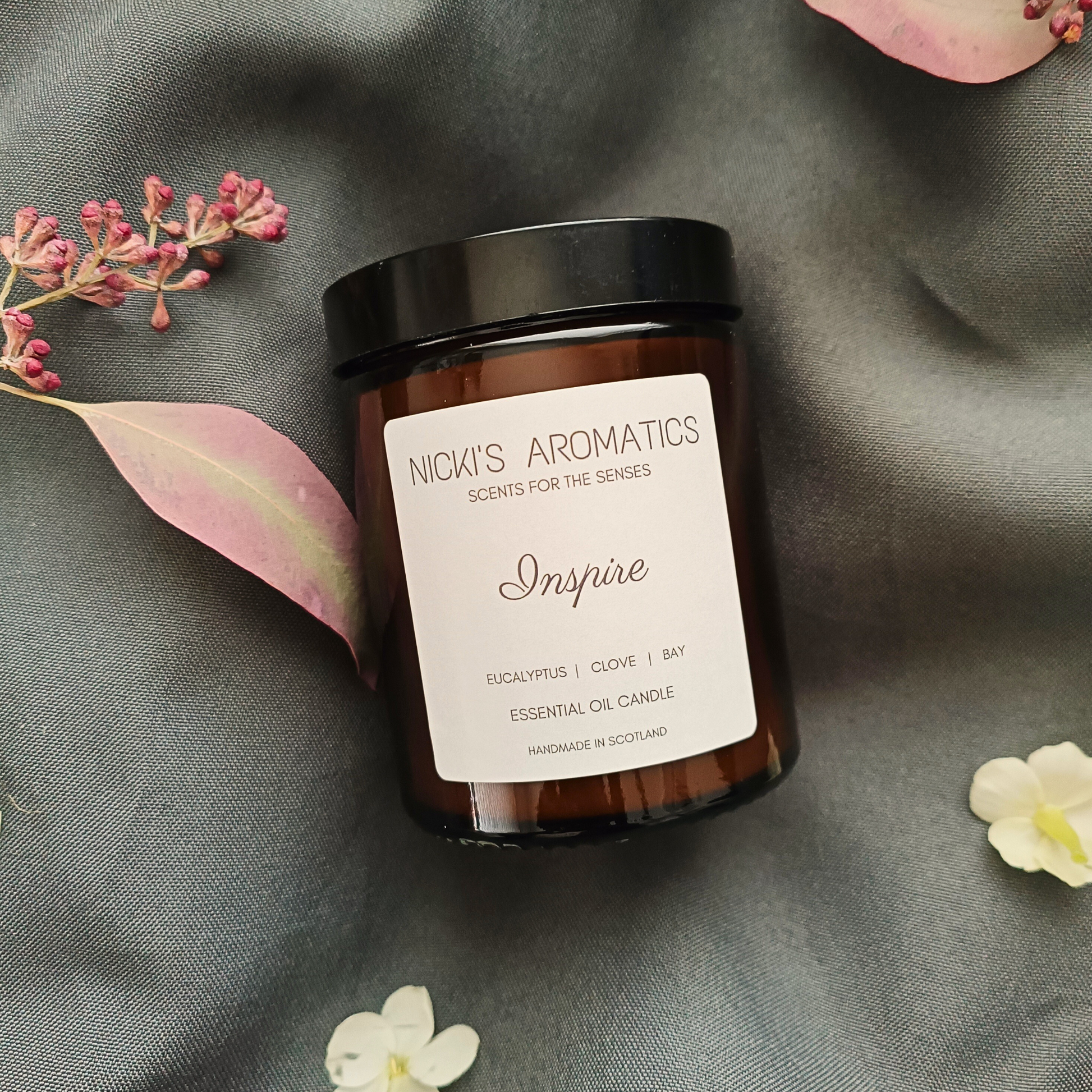 An Inspire essential oil candle in an amber glass jar resting on a grey sheet