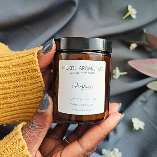 A pair of hands holding an Inspire essential oil candle in an amber glass jar