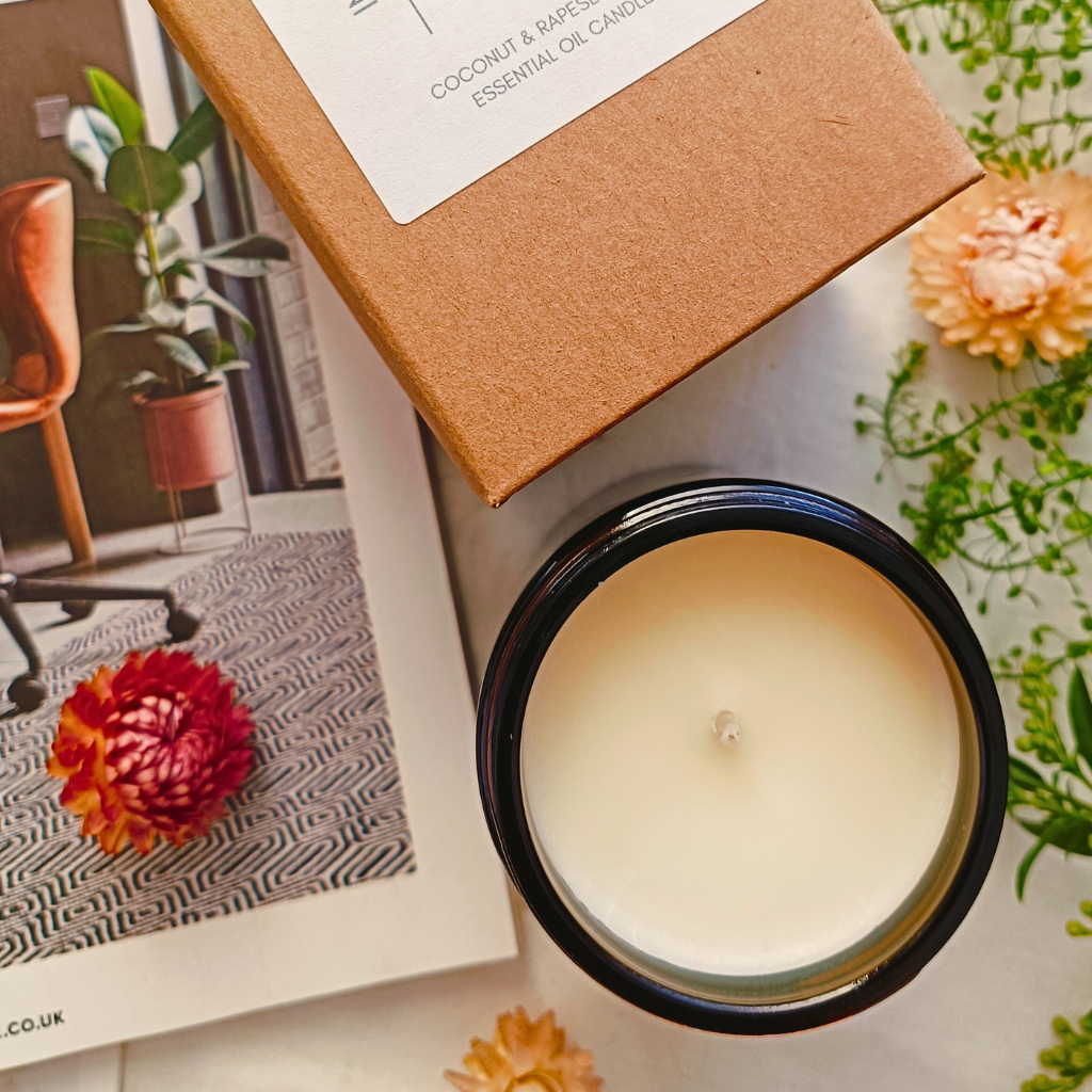 An open candle in an amber glass jar next to a packaged candle in a kraft box and an open magazine