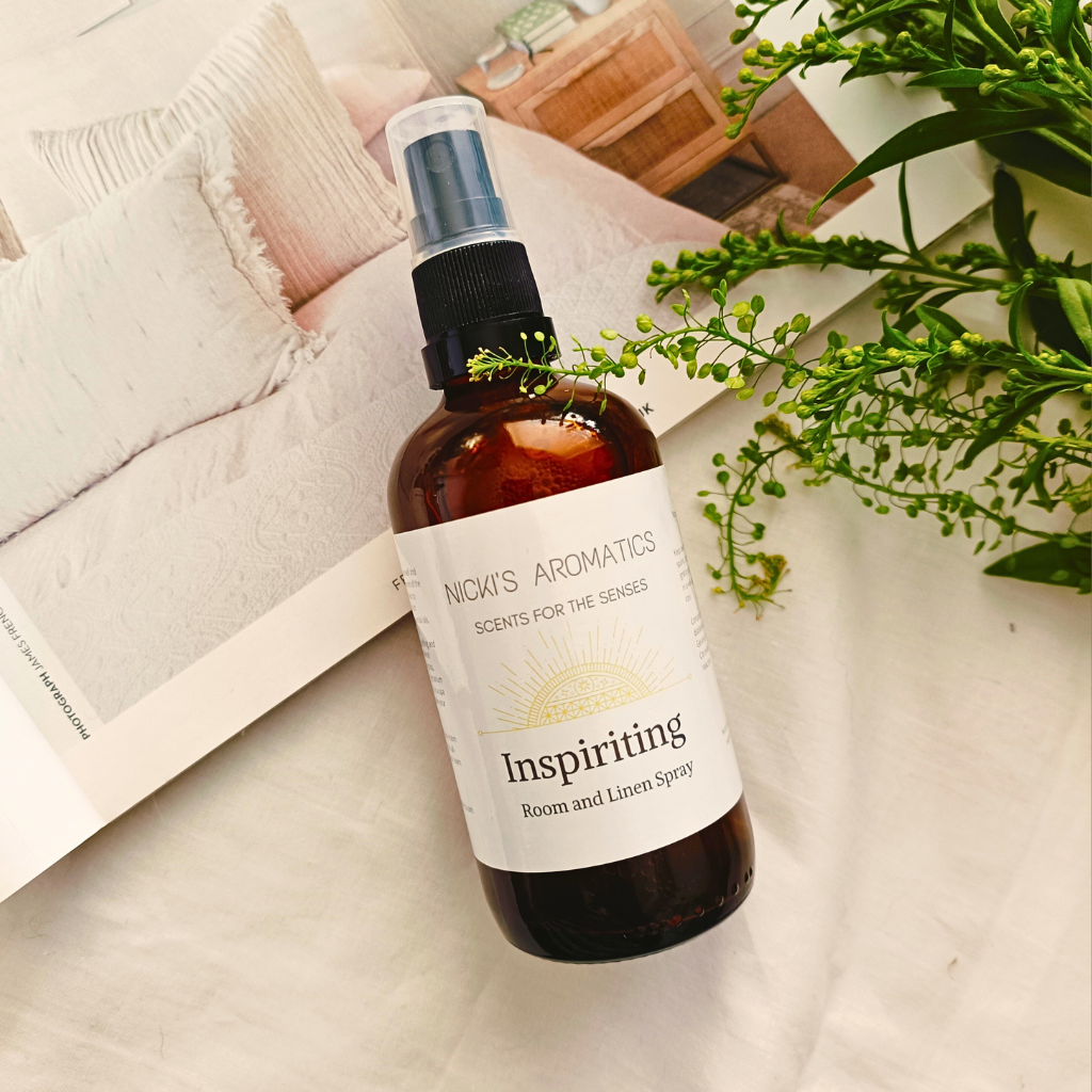 A 100ml amber glass bottle of Inspiriting essential oil room and linen spray resting on an open magazine