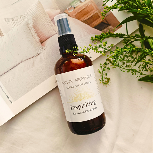 A 100ml amber glass bottle of Inspiriting essential oil room and linen spray resting on an open magazine