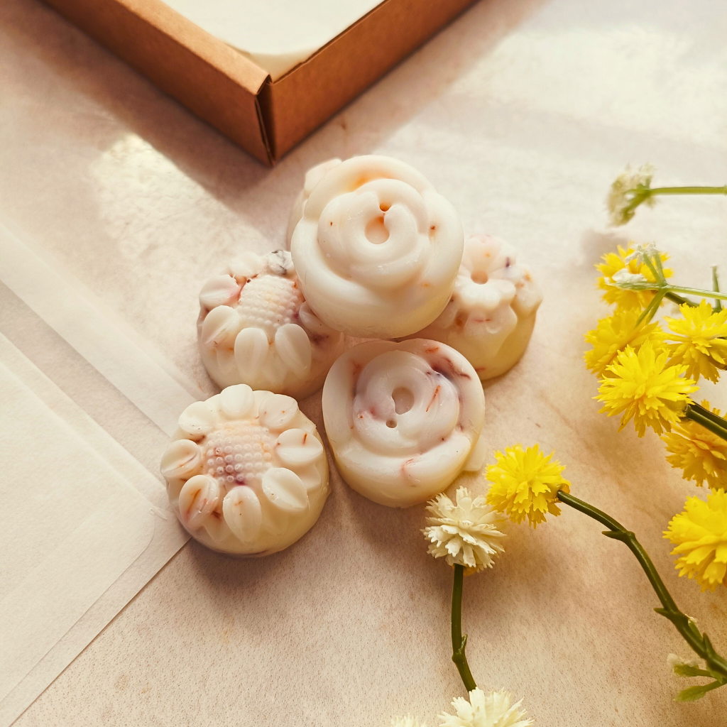 6 individual Inspiriting essential oil wax melts next to a glassine bag and flowers