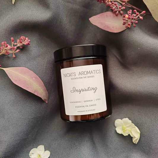 An Inspiriting essential oil candle in an amber glass jar on a grey sheet