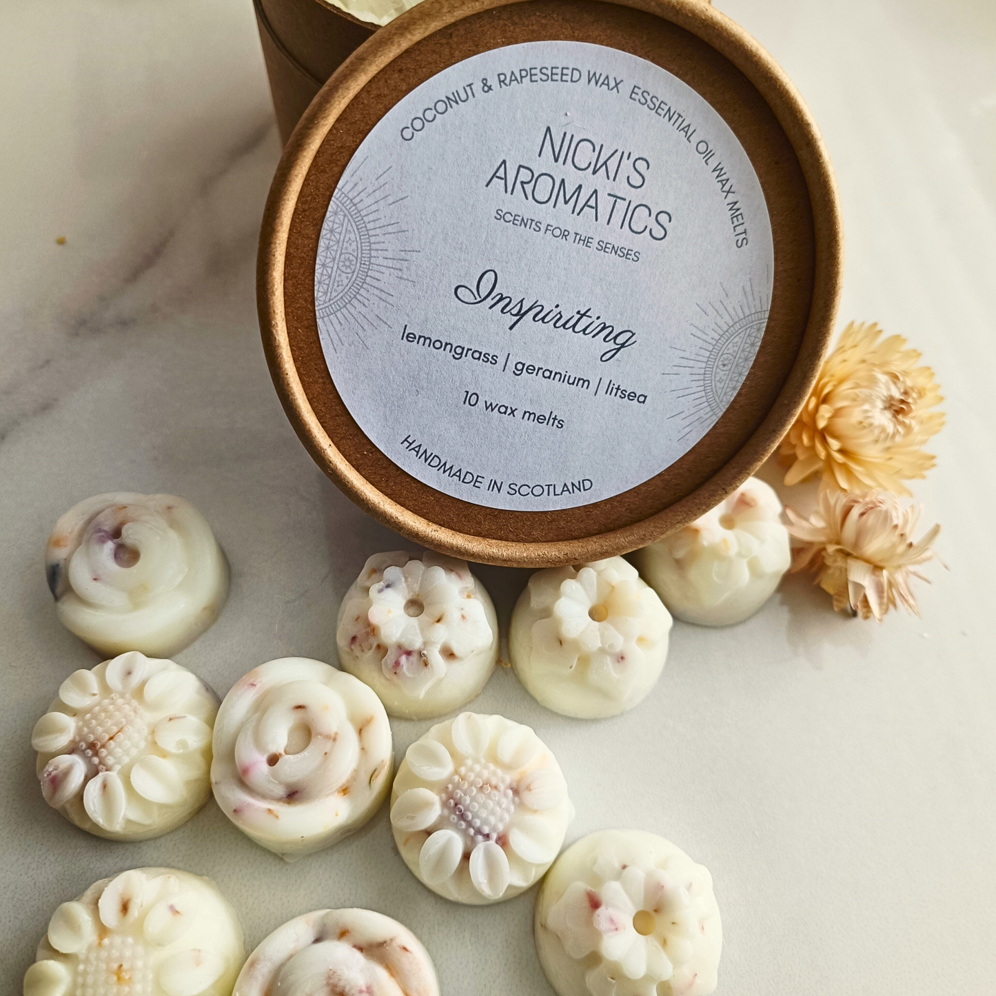 An open tub of Inspiriting essential oil wax melts with the 10 individual flower-shaped wax melts in front