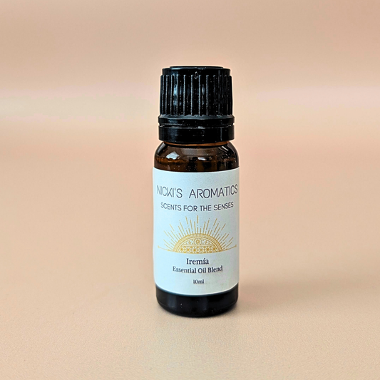 A 10ml amber glass bottle of Nicki's Aromatics 'Iremia' essential oil blend made with lemongrass, grapefruit and rosewood. With a black cap and white label, set against a warm peach background.
