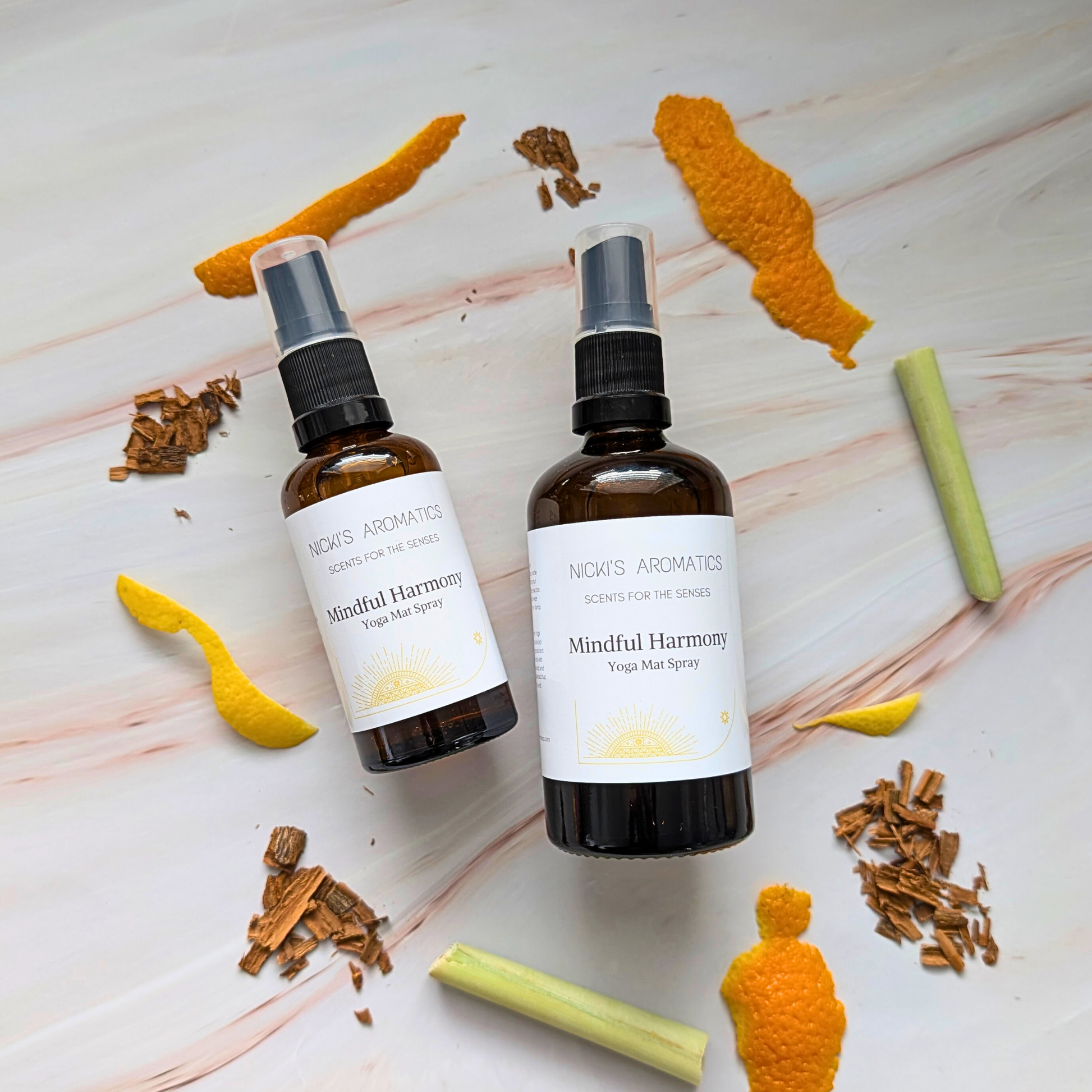 two bottles in two sized of natural yoga mat sprays in amber glass bottles surrounded by ingredients