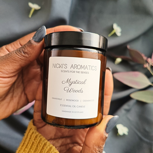 A pair of hands holding an amber glass jar of Mystical Woods essential oil candle