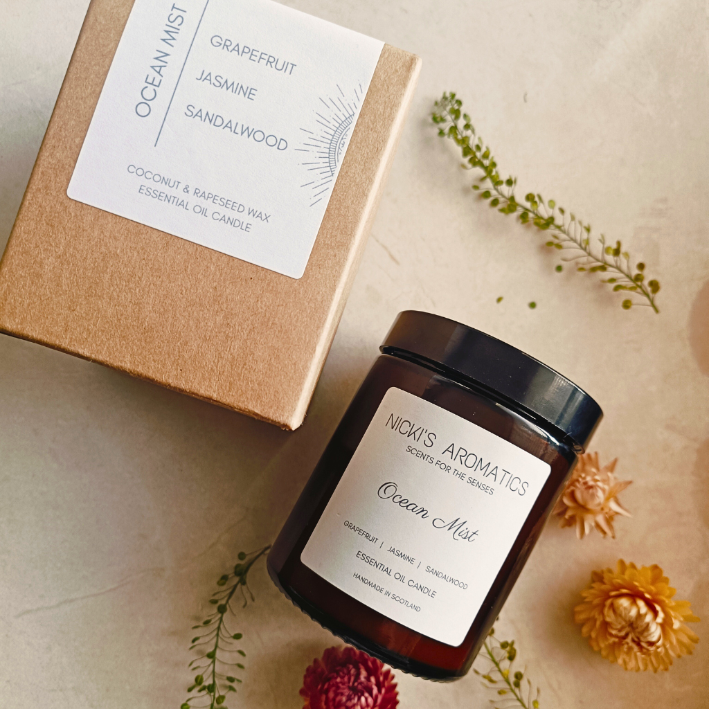 A packaged Ocean Mist essential oil candle next to a closed Ocean Mist candle in an amber glass jar