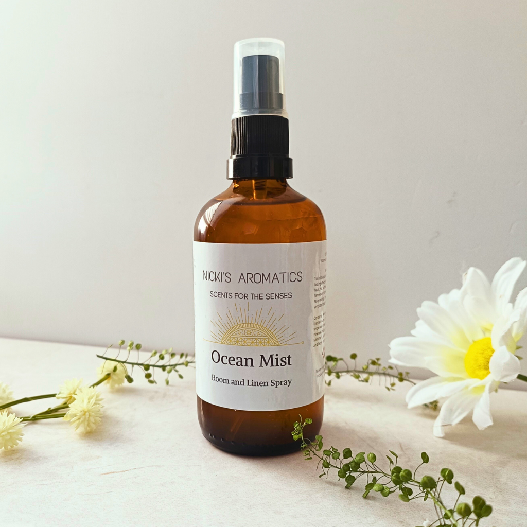 Ocean Mist essential oil room and linen spray in an amber glass bottle next to some flowers