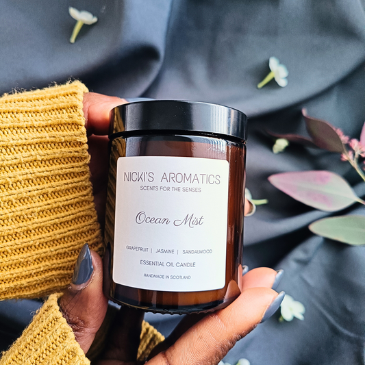 A pair of hands holding an Ocean Mist essential oil candle that is in an amber glass jar
