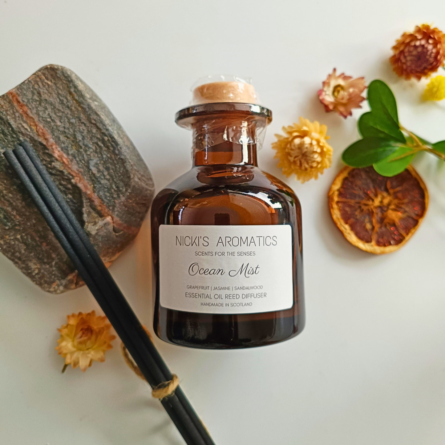 natural essential oil reed diffuser in an amber glass apothecary style bottle next to black reeds and flowers