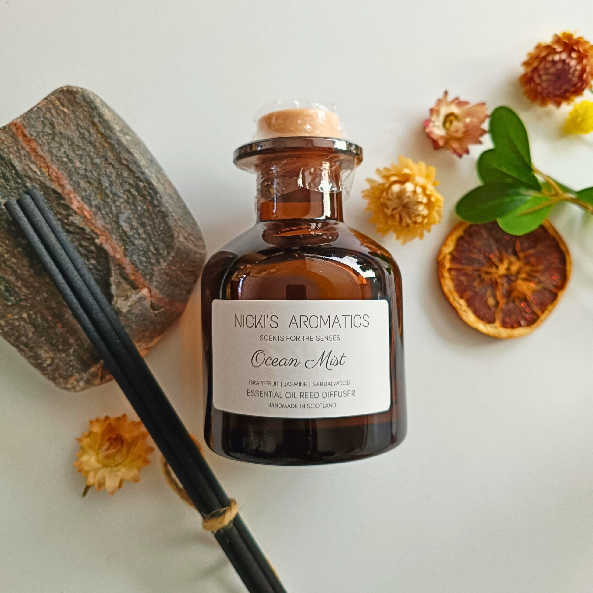 natural essential oil reed diffuser in an amber glass apothecary style bottle next to black reeds and flowers