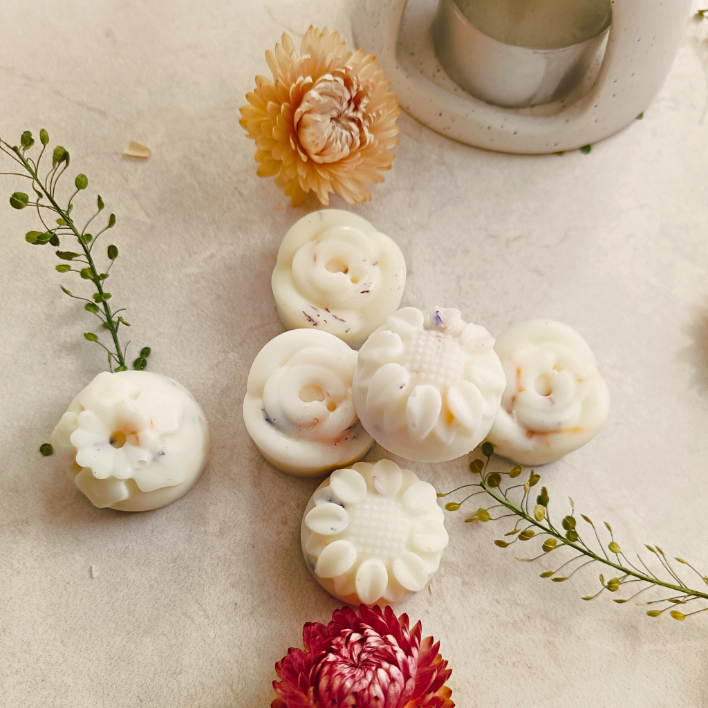 6 individual flower-shaped wax melts next to flowers