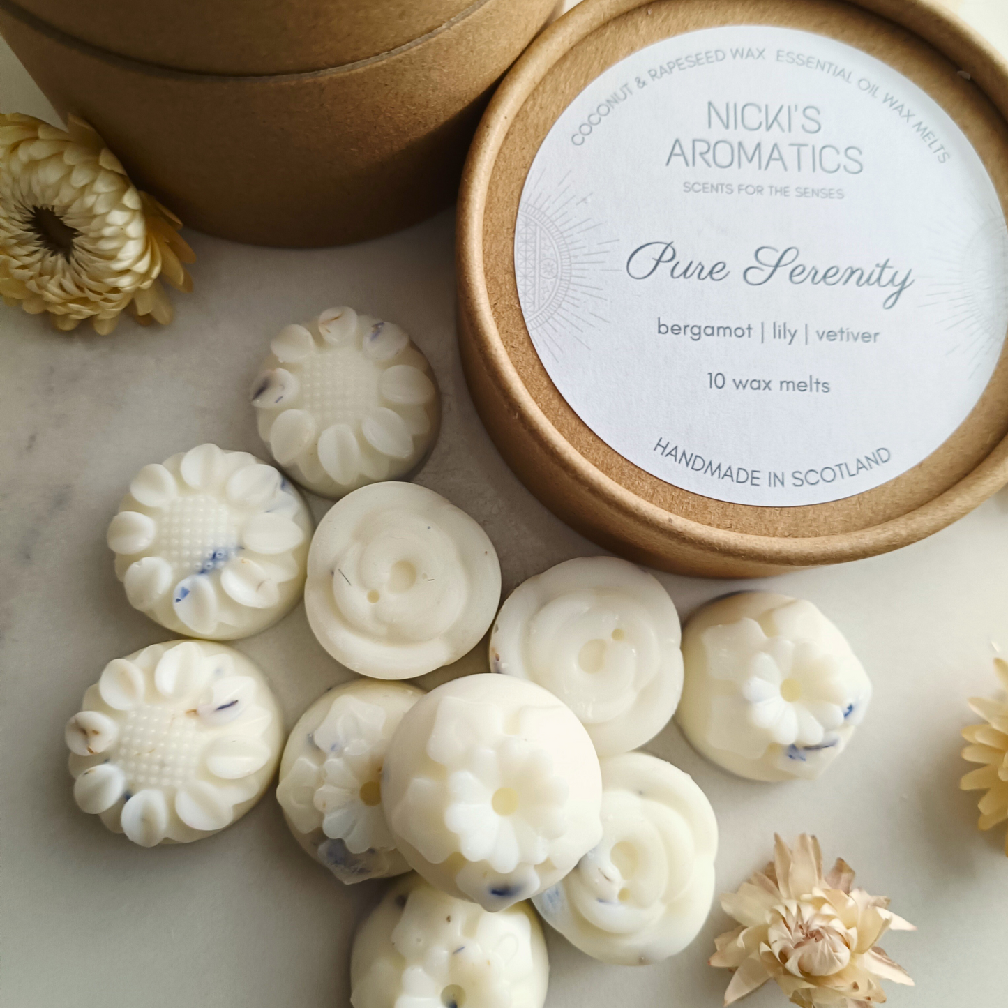 10 Pure Serenity wax melts in flower shapes next to an open kraft tube