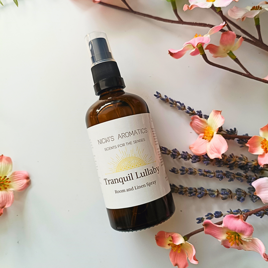 Tranquil Lullaby essential oil room and linen spray in an amber glass bottle next to flowers and dried lavender stems
