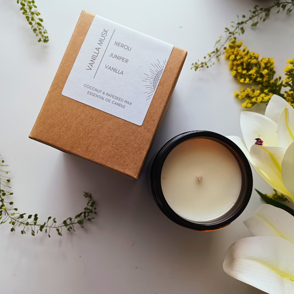 A packaged Vanilla Musk essential oil candle in a kraft box next to an open candle