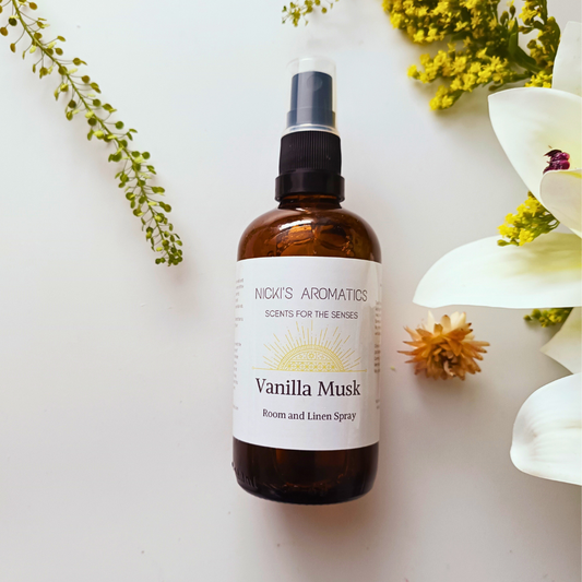 An amber glass bottle of Vanilla Musk essential oil room and linen spray on a white background with flowers