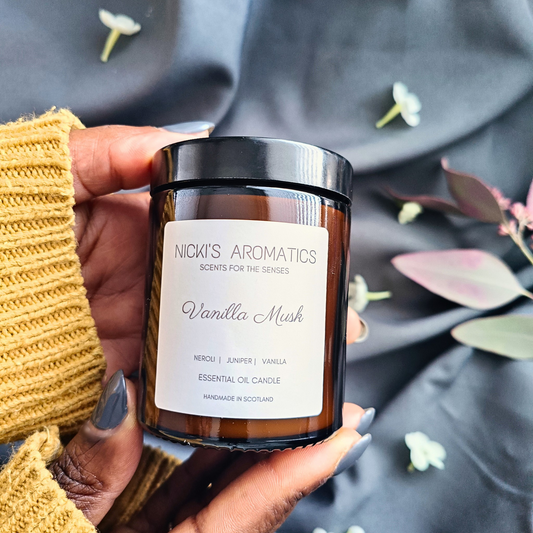 A pair of hands holding a Vanilla Musk essential oil candle in an amber glass jar