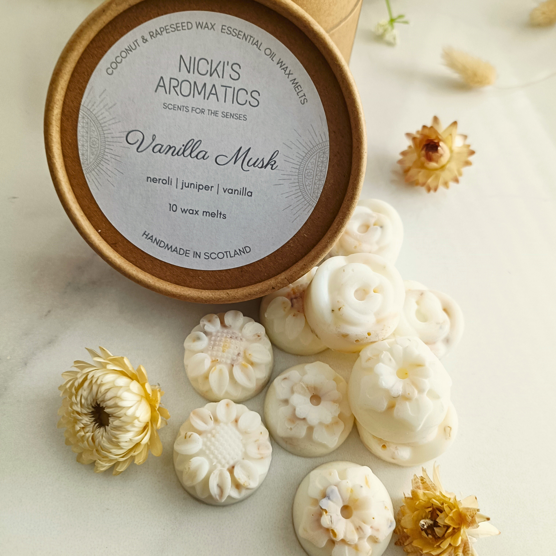 10 individual flower-shaped Vanilla Musk wax melts next to the kraft lid of the tub