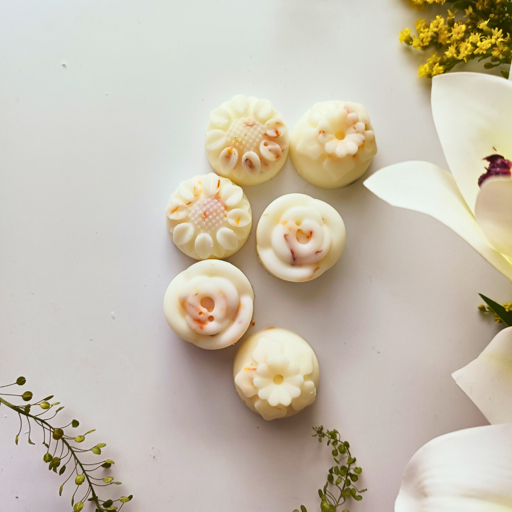 6 flower-shaped Vanilla Musk essential oil wax melts next to some flowers