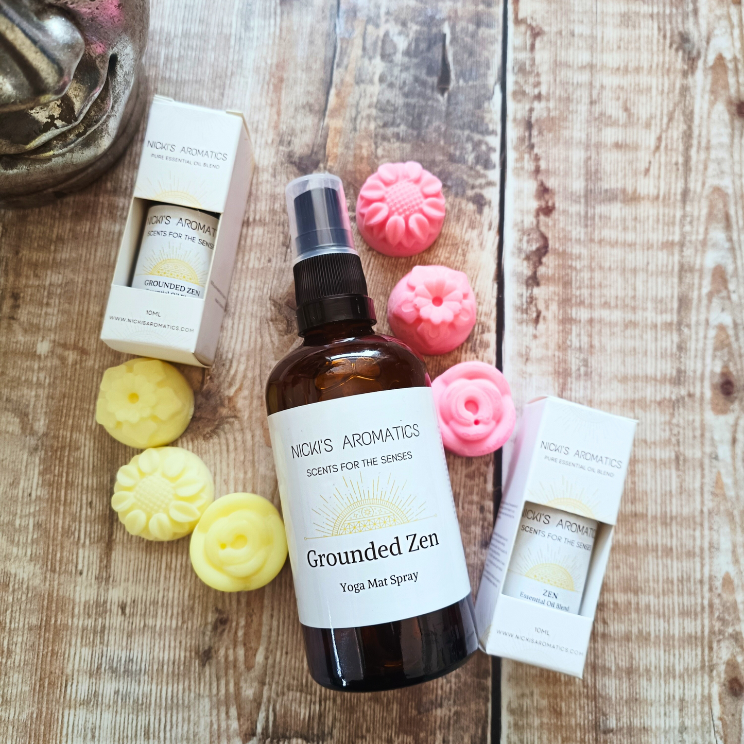 A 100ml bottle of Grounded Zen natural yoga mat spray in the middle of 6 individual flower-shaped wax melts and two 10ml essential oil blend s