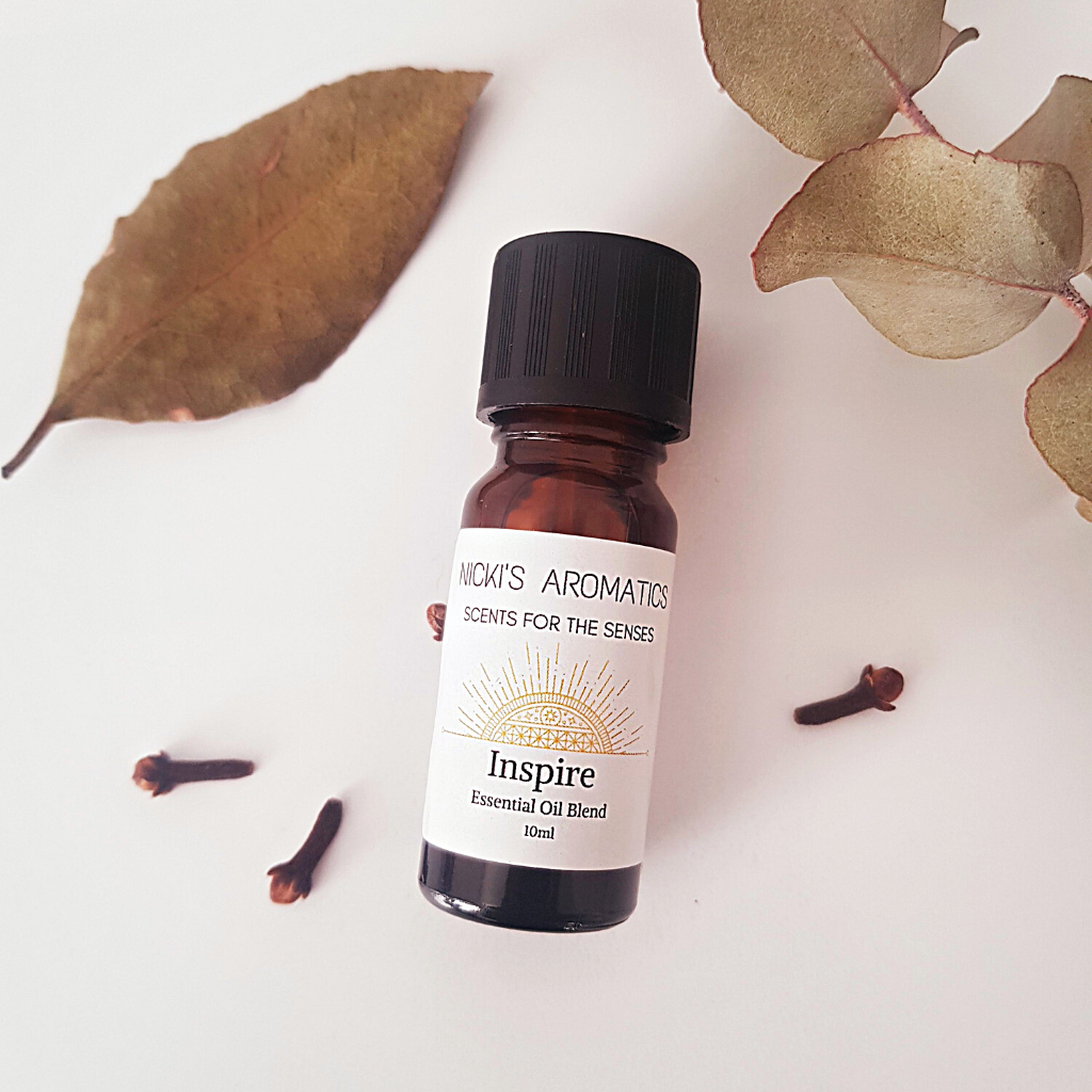 A 10ml amber glass bottle of Inspire essential oil blend surrounded by eucalyptus leaves and dried cloves