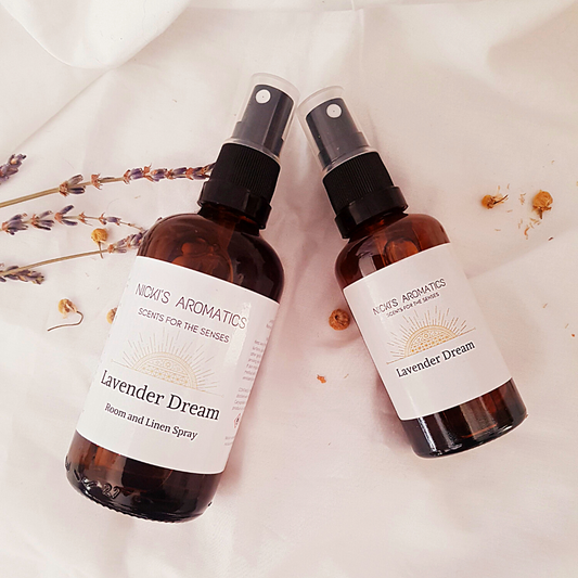 Lavender Dream room linen and pillow spray in 100ml and 50ml amber glass bottles resting on a white sheet