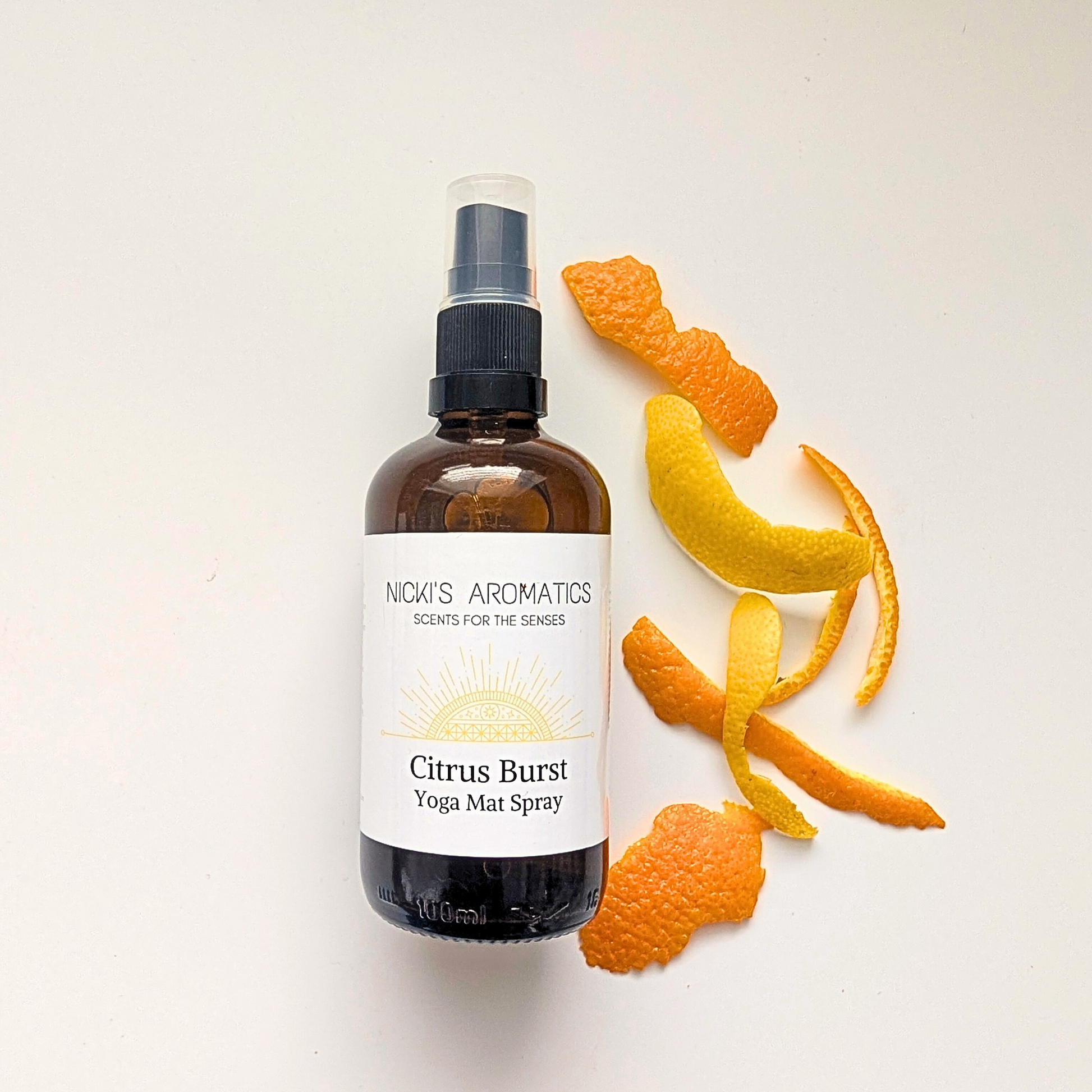 100ml amber glass bottle of Citrus Burst yoga mat spray next to some orange and lemon peel