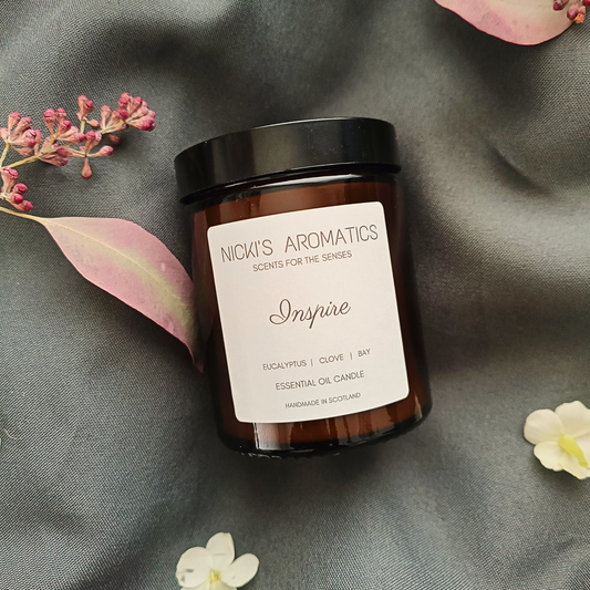 An Inspire essential oil candle in an amber glass jar resting on a grey sheet