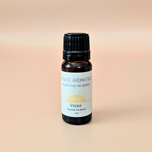 A small amber glass bottle of Nicki's Aromatics 'Vérité' essential oil blend with a black cap and white label, centered on a warm beige background.